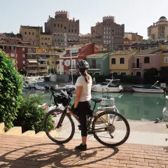 Ciclista en un puerto con casas de colores y barcos. Perfecta para descubrir las **rutas bici Valencia**.