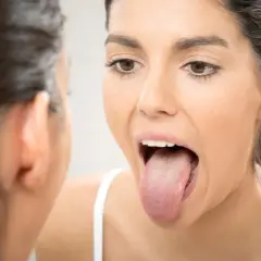 Mujer revisa su lengua en el espejo, buscando una lengua sana.