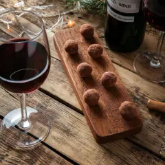 Ein Glas Rotwein und Schokoladentrüffel auf einem Holzbrett, daneben eine Flasche Wein und Lichterketten. Perfekt für einen gemütlichen Abend mit Wein und Schokolade.