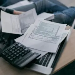 Osoba przegląda dokumenty, w tym rachunek za prąd, z kalkulatorem i laptopem.