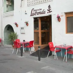 Cafetería-Bar "La Parada", un lugar acogedor donde comer en Níjar. Mesas rojas y sillas esperan en la acera.