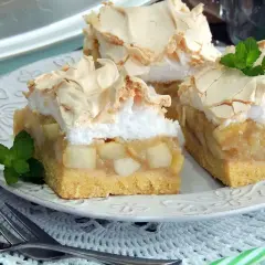 Pyszna szarlotka z bezą, z kawałkami jabłek i listkami mięty, na talerzu z widelcem.