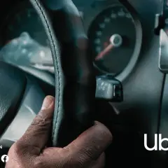 Dłoń kierowcy na kierownicy, obok smartfon z aplikacją Uber.
