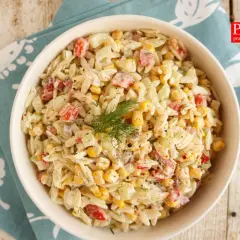 Pyszna sałatka z makaronem orzo, szynką, kukurydzą i ogórkiem, udekorowana koperkiem. Idealna na letnie dni.