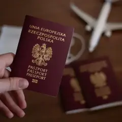 Dłoń trzyma polski paszport. Obok leżą kolejne dokumenty, maseczka i samolot. To wszystko, co potrzebne do wyrobienia paszportu i podróży.