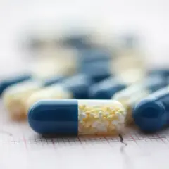 Kapsułki leku preductal mr, niebiesko-białe, leżą na papierze z liniami EKG.