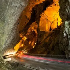 La cuevona, un túnel natural iluminado con luces cálidas, por donde pasan estelas rojas de vehículos.
