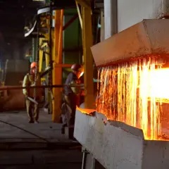 Gorący metal spływa podczas wyżarzania stali. Pracownicy w hełmach nadzorują proces w hucie.