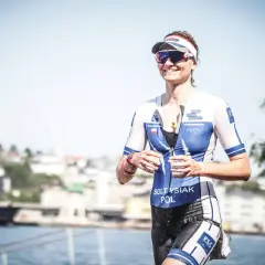 Uśmiechnięta sportsmenka w stroju do triathlonu, biegnie z kubkiem wody. To właśnie triathlon co to za dyscyplina sportu!