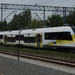 Nowy pociąg SA133-008, typu Pesa Elf, z charakterystycznym malowaniem w barwach żółto-biało-niebieskich, stoi na torach. Obok widoczny starszy wagon.