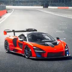 Pomarańczowy McLaren Senna z czarnym spojlerem i detalami na torze wyścigowym.