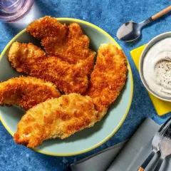 En tallrik med gyllene, krispig kyckling som ser utsökt ut. Bredvid finns en skål med krämig dipp och bestick.