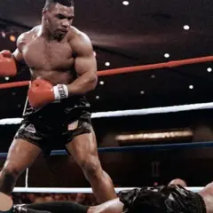 Mike Tyson, in his iconic boxing stance, stands over a fallen opponent. This image captures the intensity of a Mike Tyson workout, showcasing his power and dominance in the ring.