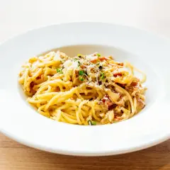 Spaghetti carbonara authentique dans une assiette blanche, garnie de lardons et de parmesan.