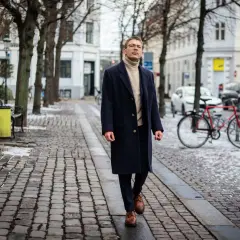 Elegancki mężczyzna w granatowym płaszczu i golfie spaceruje po zimowej ulicy. Stylowe granatowy płaszcz stylizacje na chłodne dni.