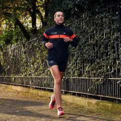 Kobieta w sportowym stroju biegnie po chodniku wśród jesiennych liści. Idealny strój, w czym biegać jesienią, zapewnia komfort i widoczność.