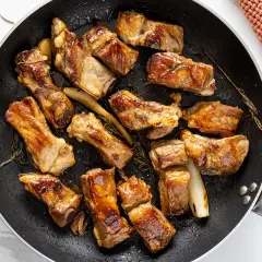 Costine di maiale in padella, dorate e succulente, con rosmarino e aglio. Un piatto invitante pronto per essere gustato.