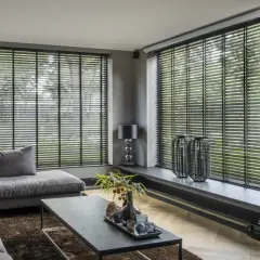Nowoczesny salon z szarą sofą, czarnymi żaluzjami czy roletami i kamiennym kominkiem.