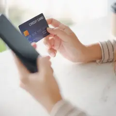Kobieta trzyma kartę kredytową i telefon, przygotowując się do płatności online. W razie problemów z transakcją, może skorzystać z procedury chargeback.