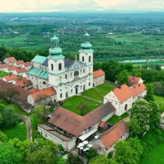 Malowniczy klasztor kamedułów Kraków na wzgórzu, otoczony zielenią, z widokiem na dolinę Wisły i miasto w oddali.