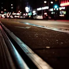 Nocne miasto z torami tramwajowymi. Światła samochodów i neonów tworzą magiczną poświatę, która umożliwia widzenie w ciemności.