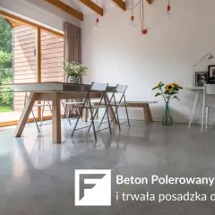 Nowoczesne wnętrze z dużymi oknami i betonem polerowanym na podłodze. W centralnej części stół jadalniany, obok biurko.