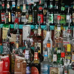 Różnorodne butelki alkoholi, od whisky po rum, stoją na półce. Zastanawiasz się, jak obliczyć procent nalewki?