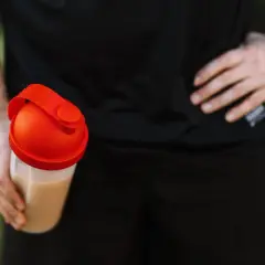 Mężczyzna trzyma shaker z napojem. Czy kreatyna zatrzymuje wodę? To pytanie nurtuje wielu sportowców.