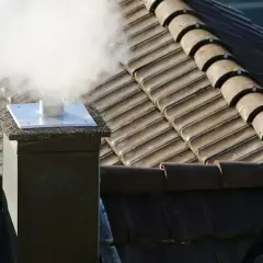 Dym wydobywający się z komina na dachu pokrytym dachówką.