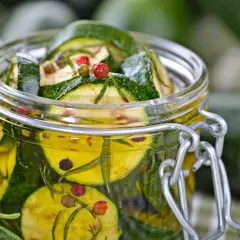 Ein Glas mit eingelegten Zucchini, Kräutern und bunten Pfefferkörnern. Perfekt für den Sommer!