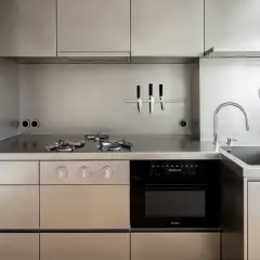 Cucina moderna con piano cottura a gas, forno, lavello e utensili appesi, tutto in lucido acciaio inox 18/10.