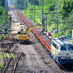 Gleisbauarbeiten: Bagger beladen einen Güterzug mit Schotter.