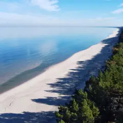 Szeroka, piaszczysta plaża Mierzei Wiślanej z lasem sosnowym po prawej stronie i spokojnym morzem.