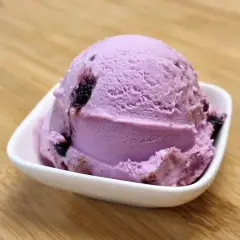 Ein Löffel Amarena-Eis mit Fruchtstückchen, das leicht nach Alkohol duftet, in einer weißen Schale auf Holzuntergrund.