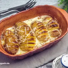Gerichte mit Kartoffeln: Hasselback-Kartoffeln in cremiger Sauce, goldbraun gebacken und mit Käse überbacken, serviert in einer Terrine.