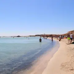 Słoneczna plaża Elafonisi z turkusową wodą, piaskiem i ludźmi odpoczywającymi pod parasolami.