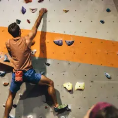 Mężczyzna wspina się po ścianie w hali do boulderingu. To świetny sposób na aktywność fizyczną i rozwijanie siły.