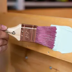 Holzbank streichen ohne schleifen: Ein Pinsel mit hellblauer Farbe wird über das Holz geführt.
