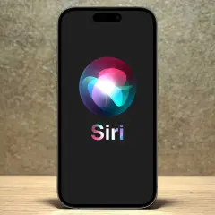 Na ekranie telefonu widnieje logo Siri, które wygląda jak kolorowa, świetlista kula.