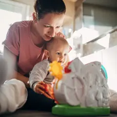 Mama bawi się z 5-miesięcznym dzieckiem, które z zaciekawieniem ogląda kolorową zabawkę.