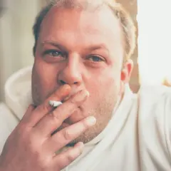 Hombre con cigarrillo en la mano, con el pelo rubio y ojos azules. Fumar hace que se te caiga el pelo.
