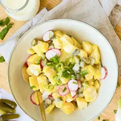 Ein cremiger veganer Kartoffelsalat mit Mayo, Radieschen und Gurken, garniert mit Frühlingszwiebeln.