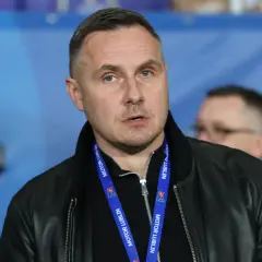 Mężczyzna w czarnej kurtce z niebieską smyczą z napisem "MOTOR LUBLIN" na szyi.