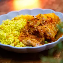 Herzhaftes Sudado de Pollo mit gelbem Reis und Erbsen, serviert in einer weißen Schale auf einem Holztisch.