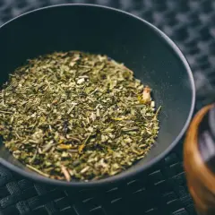 Suszone liście i gałązki, z których jest yerba mate, w czarnej miseczce obok tykwy.