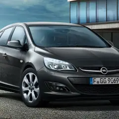 Ciemnoszary Opel Astra J lift z tablicą rejestracyjną F GG 9069 stoi przed nowoczesnym budynkiem.