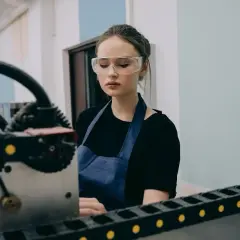 Młody pracownik produkcji w okularach ochronnych i fartuchu pracuje przy maszynie.