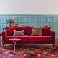 Ein rotes Samtsofa mit braunen Kissen vor einer blau getäfelten Wand. Welche Farbe passt zu Rot? Braun und Blau sind eine tolle Wahl!