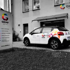 Samochód firmowy GRIMP z kolorowym brandingiem, gotowy do wycofania z firmy. Obok tablica informacyjna z usługami.