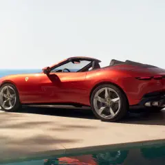 Czerwony Ferrari Spider z otwartym dachem, zaparkowany przy basenie z widokiem na morze.